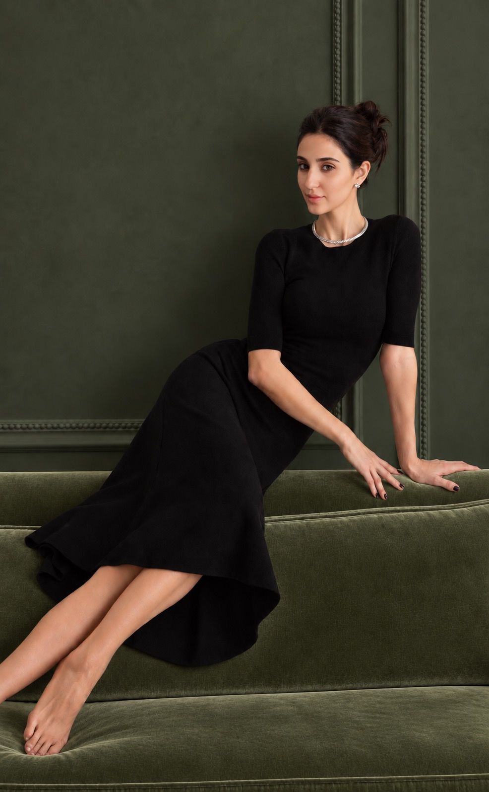 Helia seated on a green sofa in front of a green wall